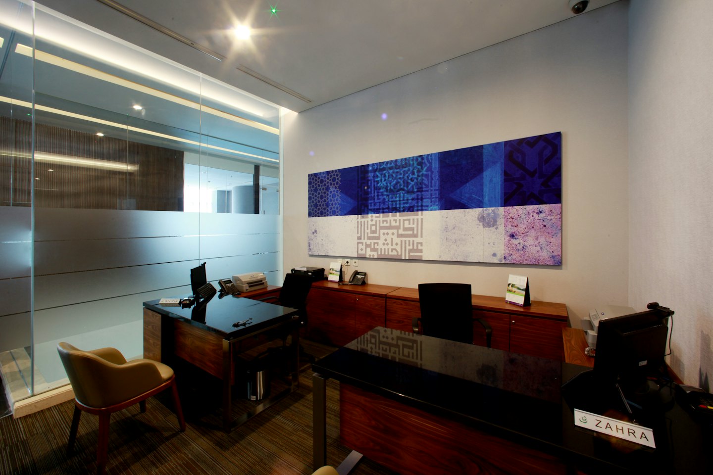 Two dark wooden desks sit in front of abstract wall art.