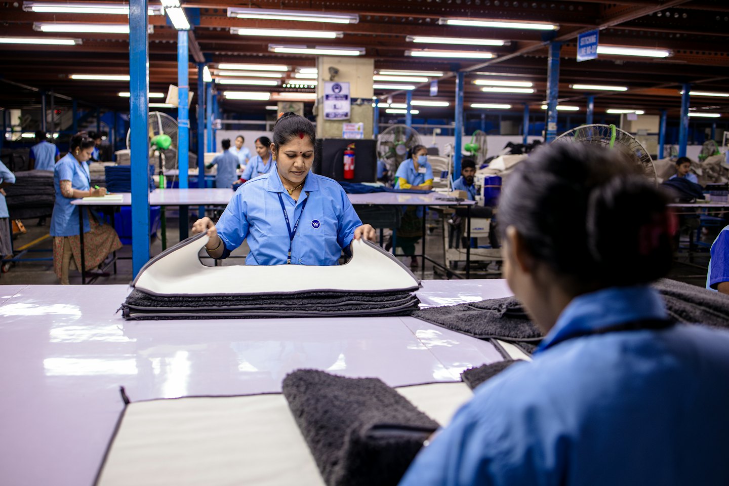 Woman in blue uniform inspecting textile product in factory.