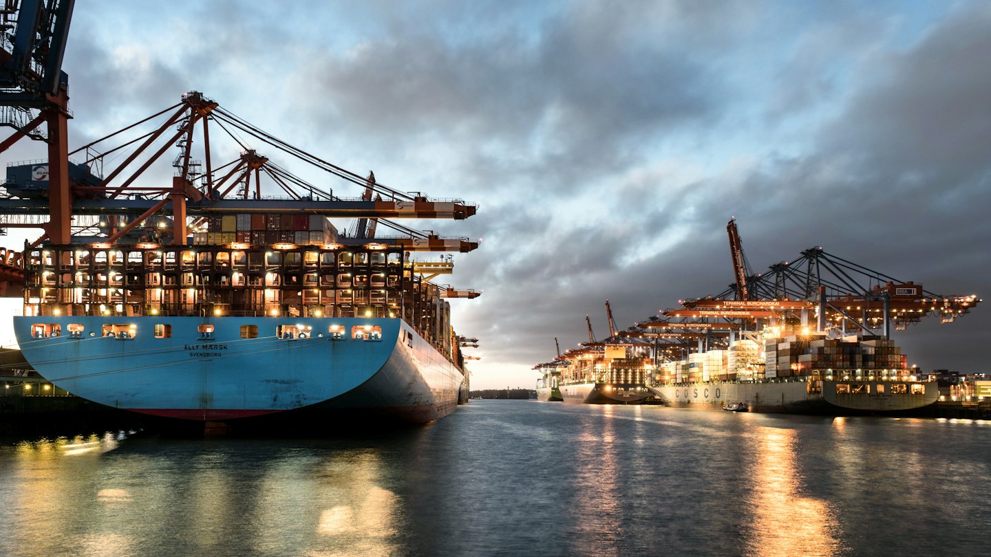 Container ships being loaded by cranes at a port at night.