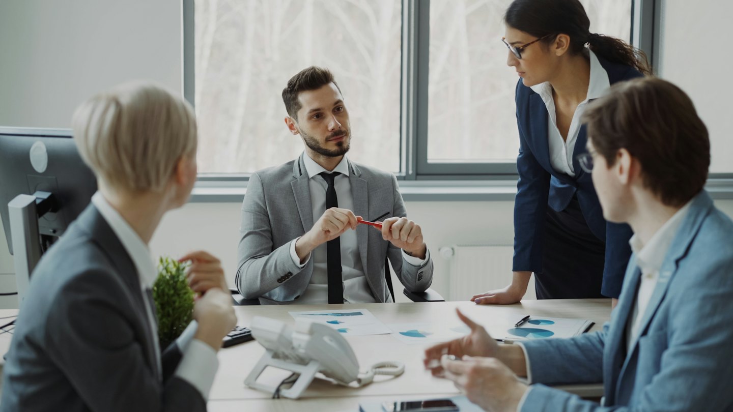 Business professionals discuss plans around a conference table.